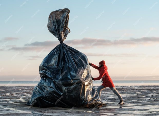 woman-pushes-huge-black-trash-bag-shore_426900-1019
